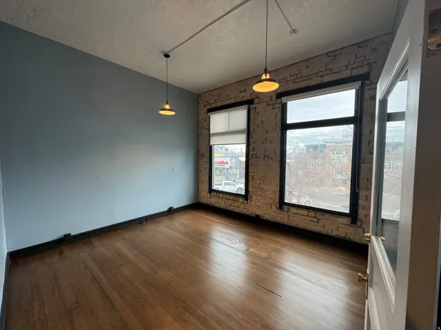 Unfurnished dining area featuring dark wood finished floors, a textured ceiling, and brick wall