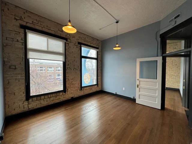 Unfurnished dining area with brick wall, a textured ceiling, and dark wood-style floors