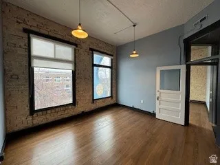 Unfurnished dining area featuring dark wood-style floors, a textured ceiling, brick wall, and an accent wall