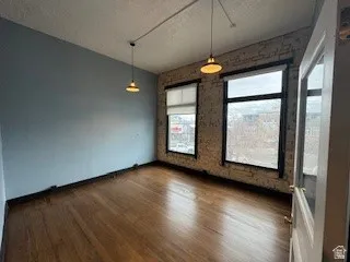 Unfurnished dining area with dark wood-style floors, brick wall, and a textured ceiling