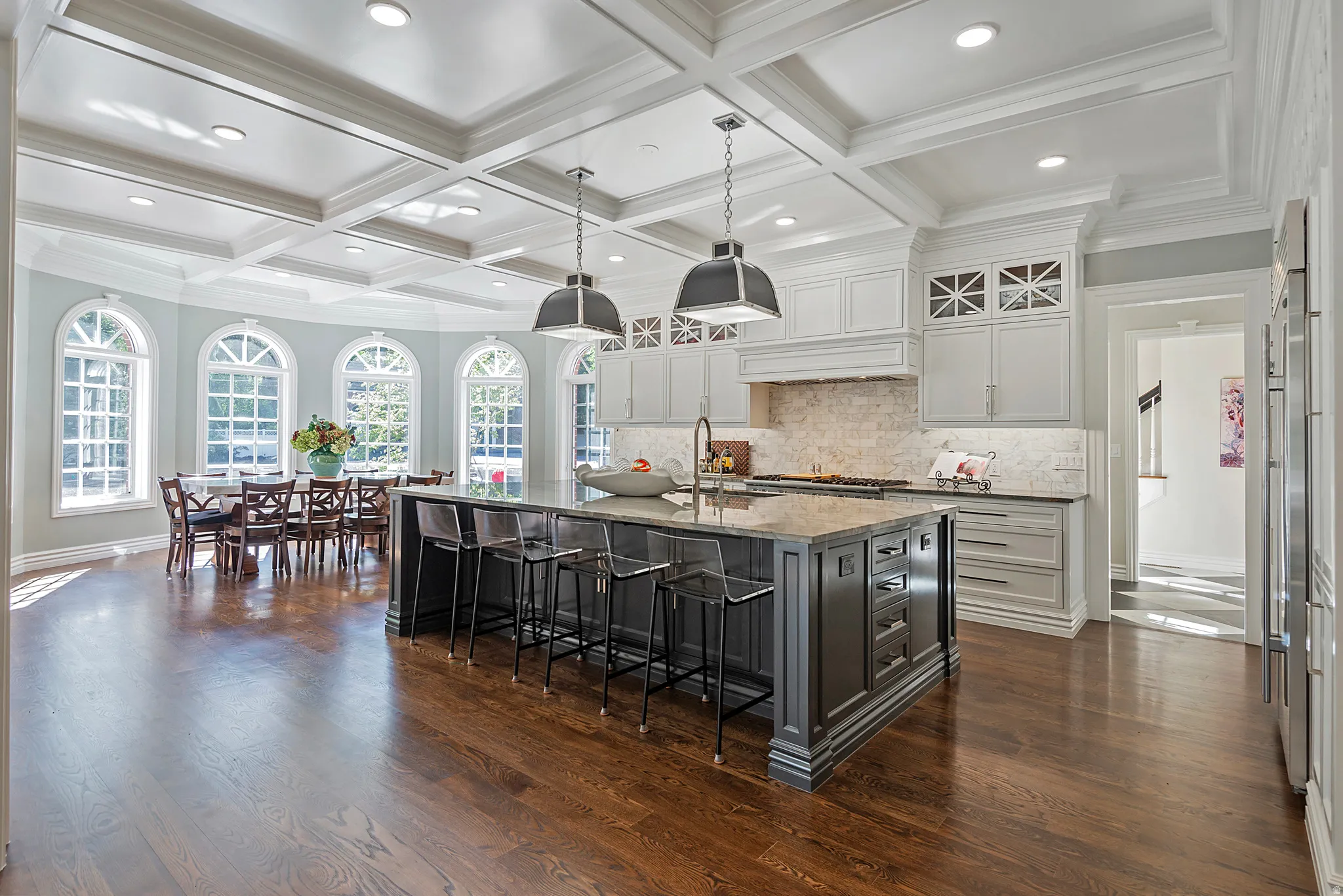 Light and airy kitchen with two tone cabinetry, beautiful pendant light fixtures, a breakfast bar, a large island, coffered ceiling and wood floors
