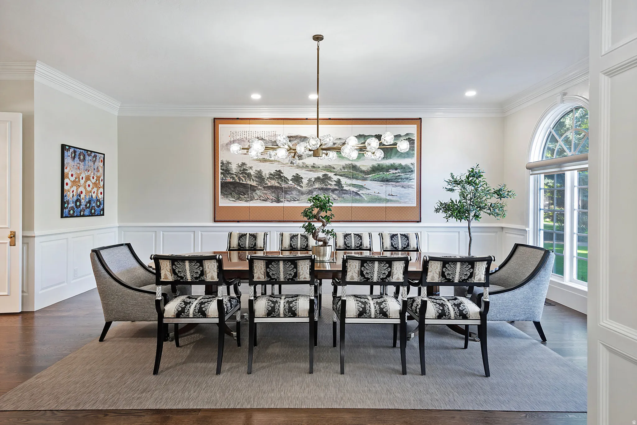Expansive formal dining room featuring wainscoting, crown molding, wood flooring, and lovely chandelier.
