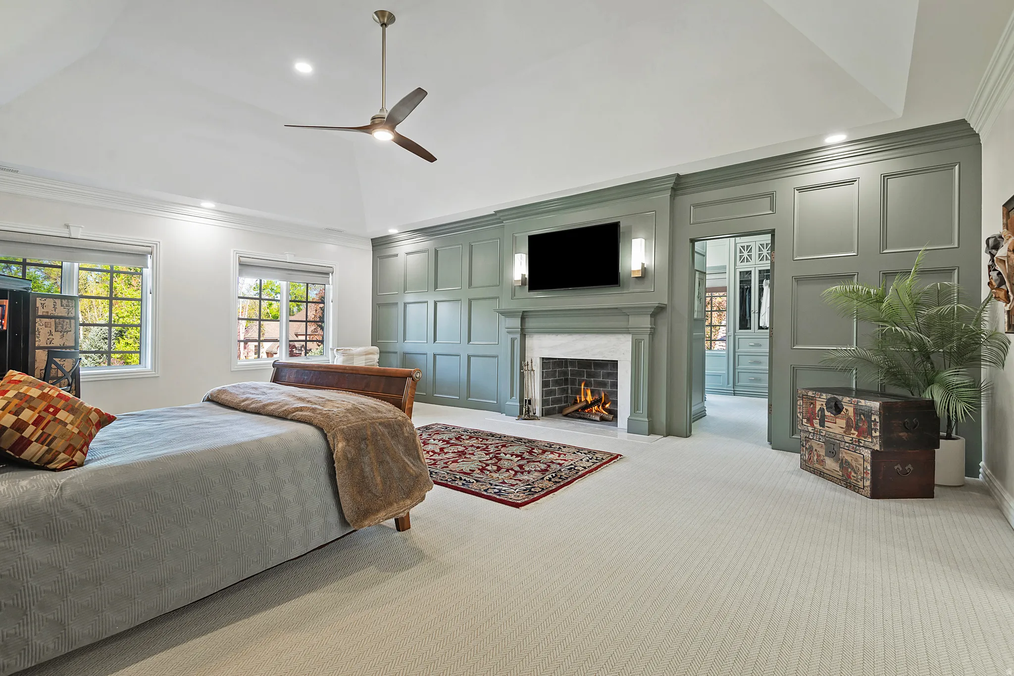 Expansive primary bedroom with ornamental decorative molding, a fireplace with flush hearth, light colored upscale carpet, and recessed lighting,