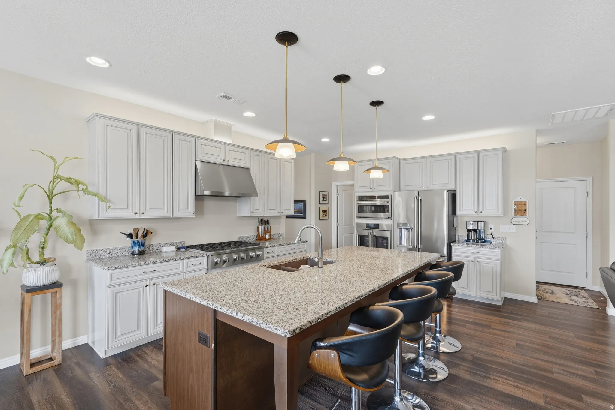 Kitchen with a breakfast bar, light stone counters, dark wood-style floors, and two tone cabinets