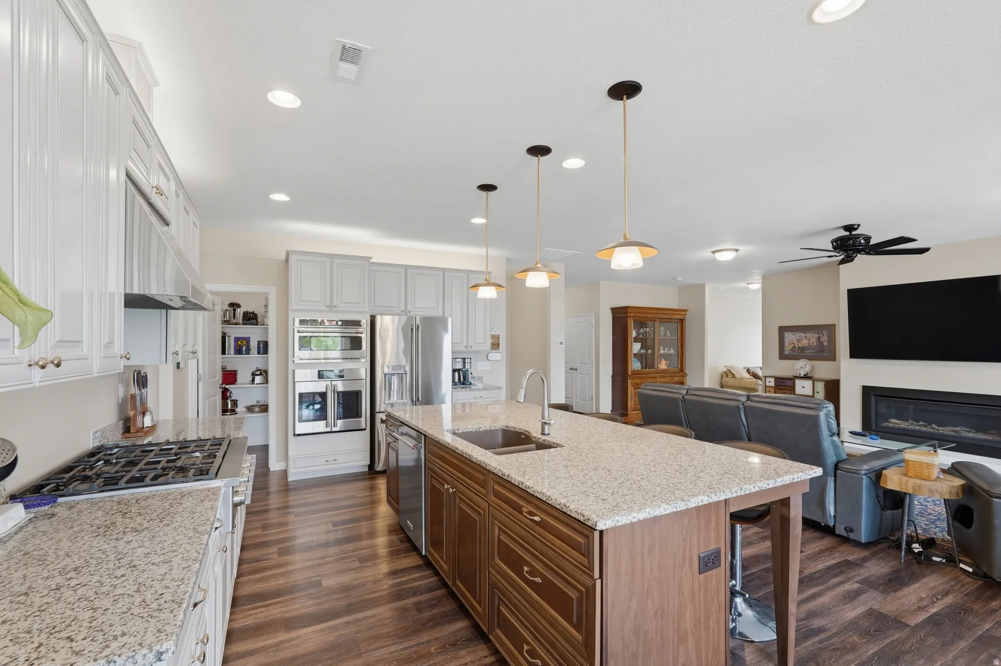 Two tone kitchen featuring light stone countertops, a breakfast bar area, open floor plan, two tone cabinetry, and an island with sink