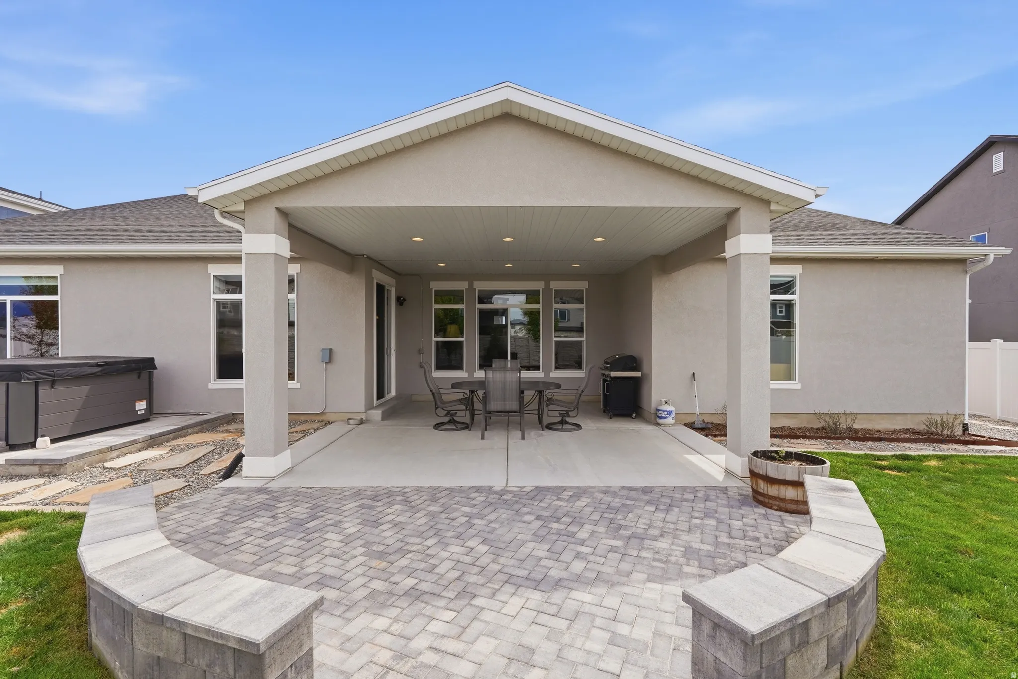 Back of house with stucco siding, outdoor dining area, a patio area, and a hot tub