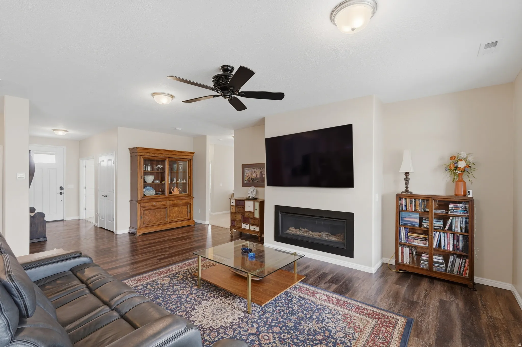 Living area featuring ceiling fan, a glass covered fireplace, and dark wood-type flooring
