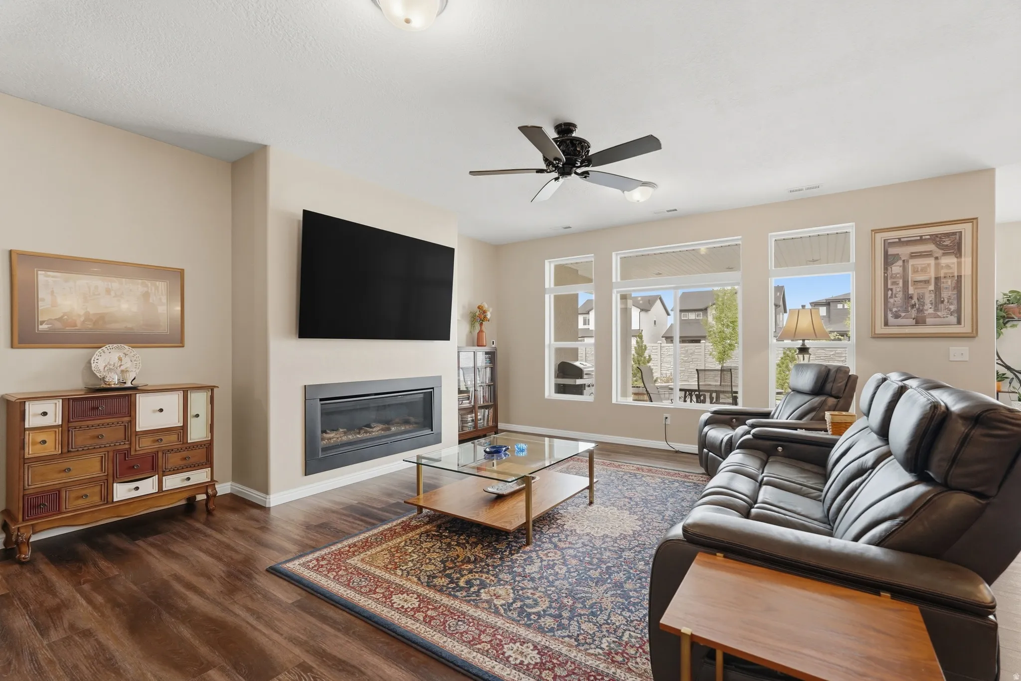 Living room featuring a glass covered fireplace, a ceiling fan, and dark wood-style floors