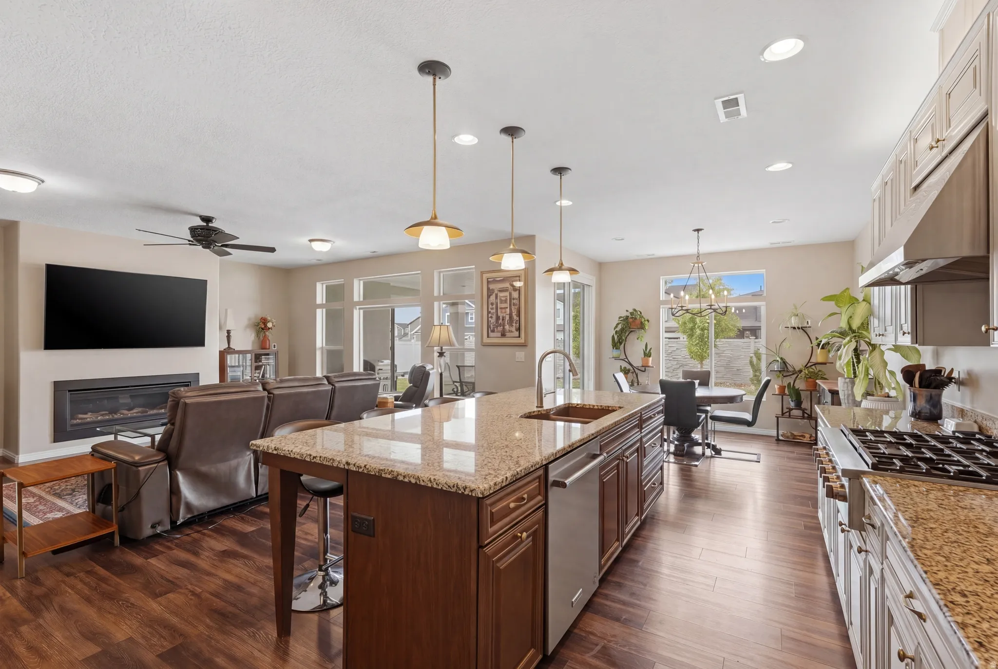 Dual tone kitchen with light stone countertops, open floor plan, stainless steel appliances, a glass covered fireplace, and dark wood-style flooring