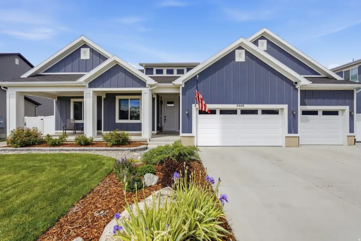 View of front of house with board and batten siding, an attached garage, concrete driveway, a porch, and a front lawn