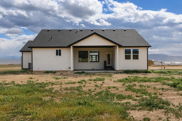 Back of property with a shingled roof, stucco siding, and a patio area