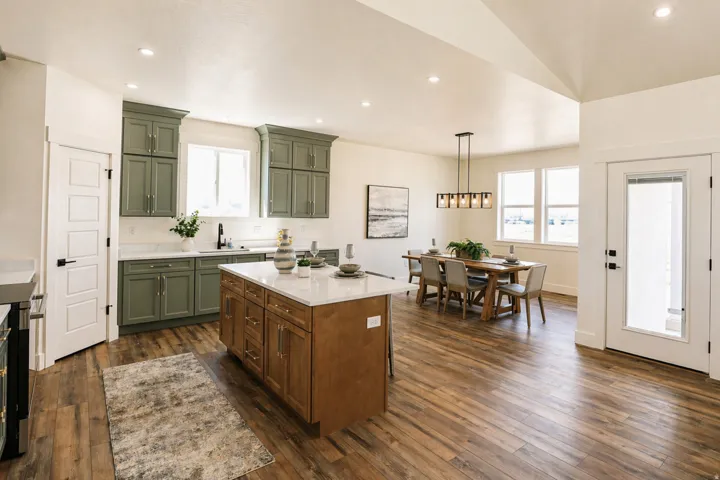 Kitchen featuring green cabinets, dark wood-style floors, light stone counters, decorative light fixtures, and a kitchen island