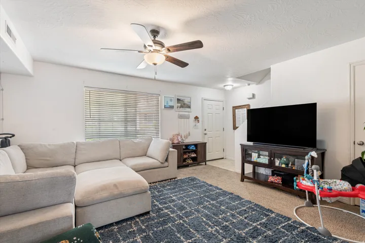 Living area featuring ceiling fan, a textured ceiling, and light carpet