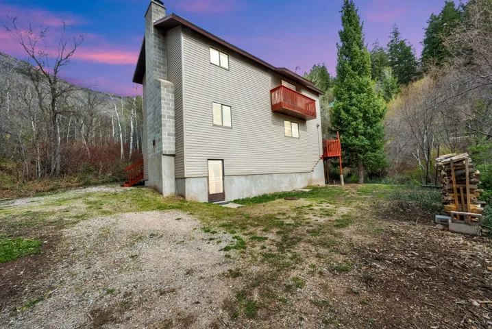 Back of house at dusk with a chimney and view of wooded area