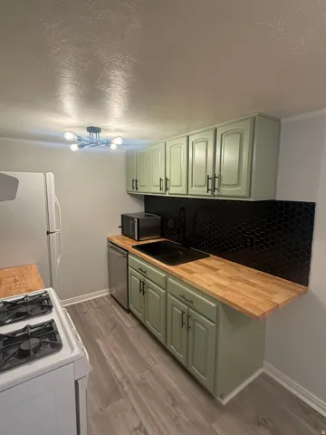Kitchen featuring white appliances, green cabinets, a textured ceiling, dark wood-style flooring, and butcher block counters