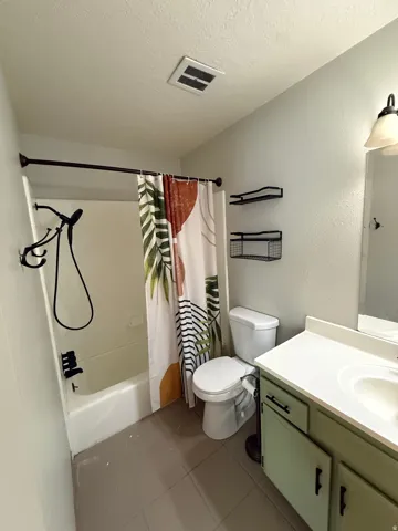 Bathroom with vanity, shower / bath combination with curtain, dark tile patterned floors, a textured ceiling, and a textured wall