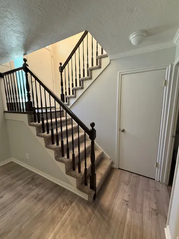 Stairway with a textured ceiling, wood finished floors, and crown molding