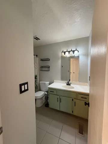 Full bath with vanity, a textured ceiling, light tile patterned flooring, and a shower with curtain