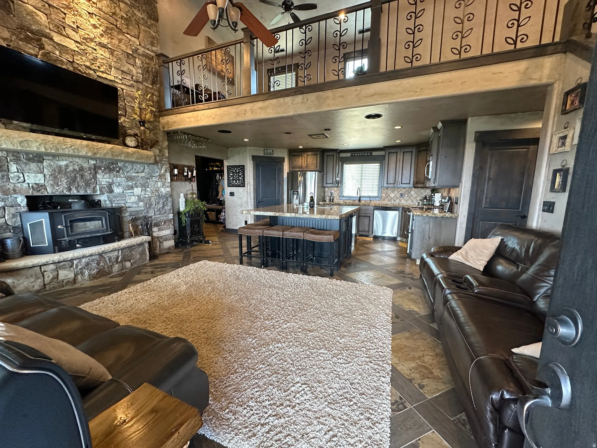Living room with a high ceiling, ceiling fan, stone tile floors, recessed lighting, and a wood stove