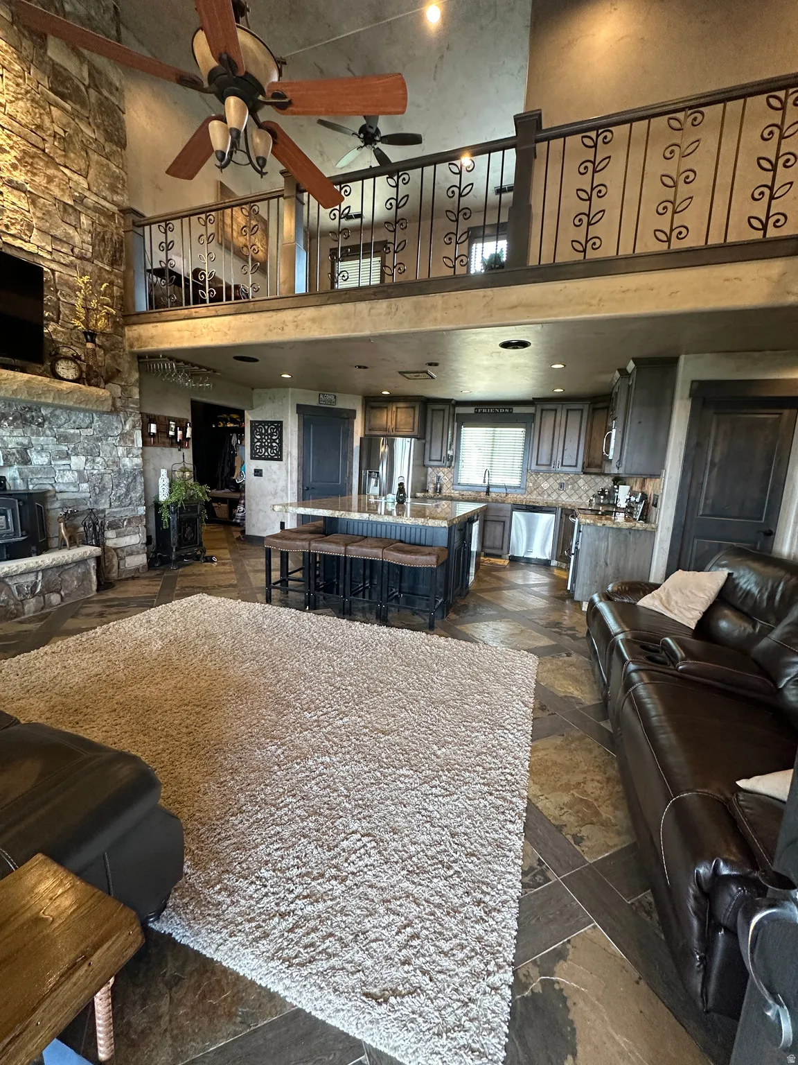 Living area with a high ceiling, stone tile flooring, ceiling fan, and a stone fireplace
