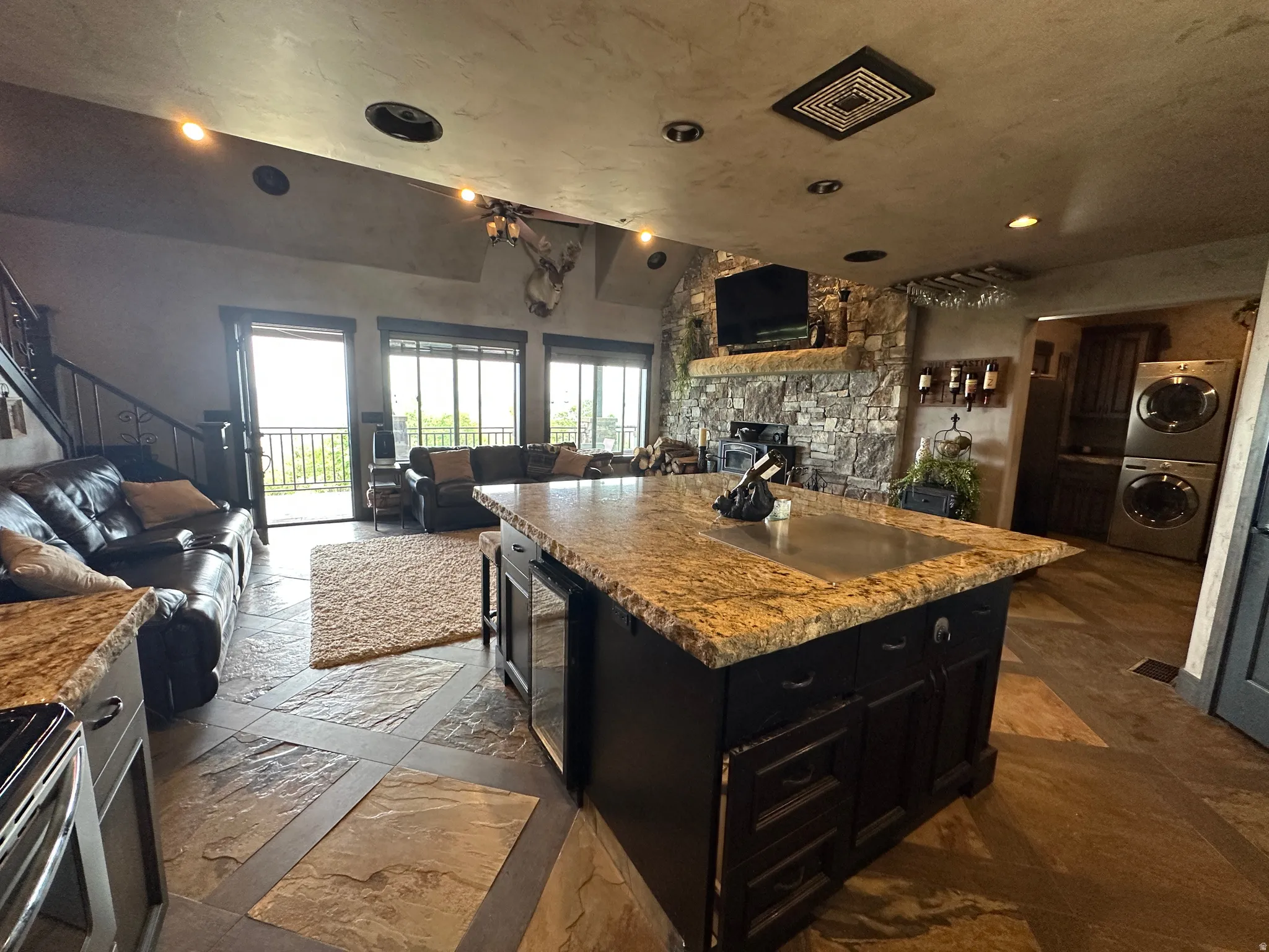 Kitchen featuring dark cabinetry, open floor plan, stone tile flooring, stainless steel stove, and stacked washer and clothes dryer