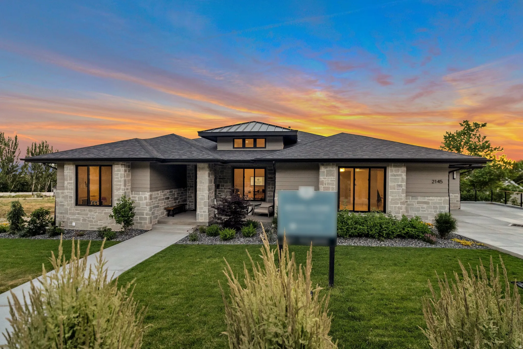 Prairie-style home featuring stone siding, a lawn, a shingled roof, and a standing seam roof
