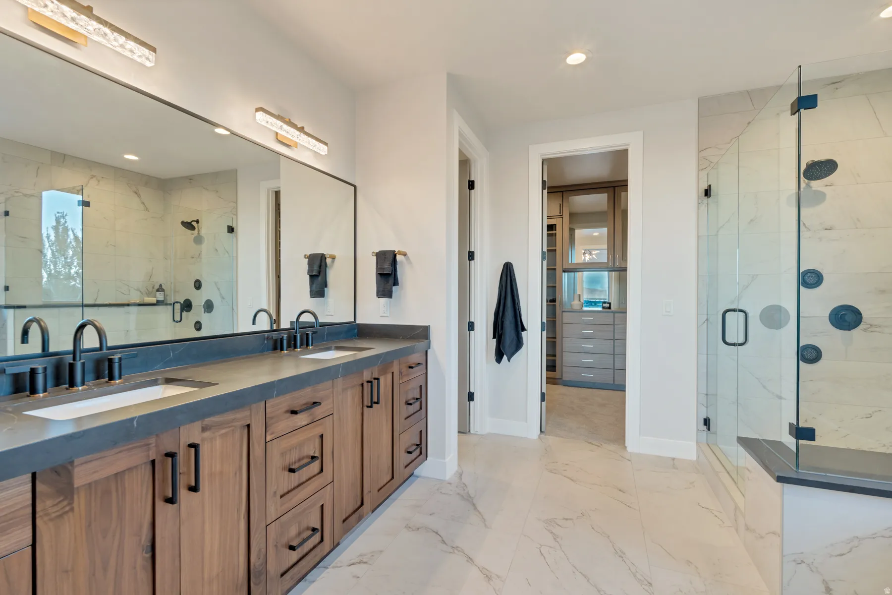 Bathroom with double vanity, a marble finish shower, recessed lighting, and light marble finish floors