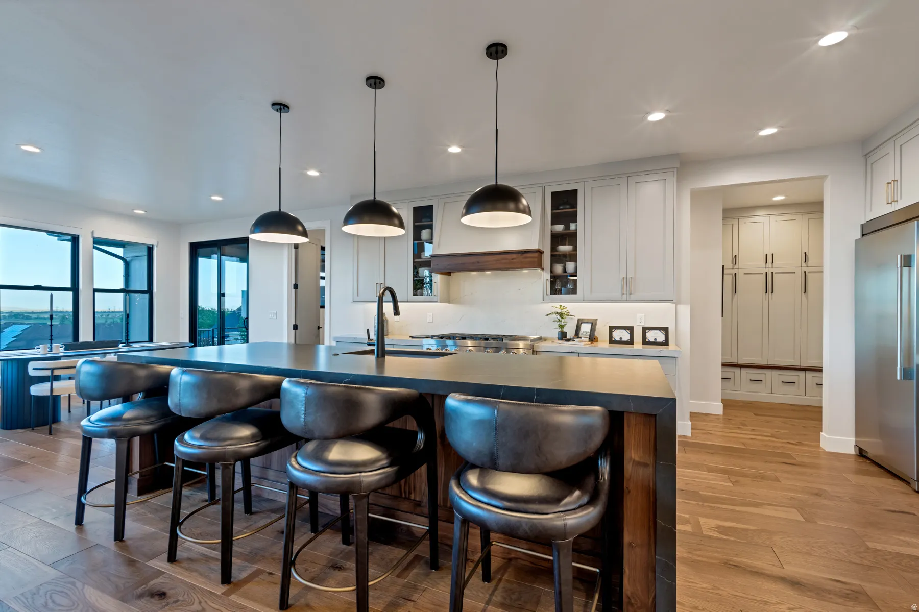 Kitchen featuring glass insert cabinets, high quality fridge, pendant lighting, light wood-style floors, and a breakfast bar