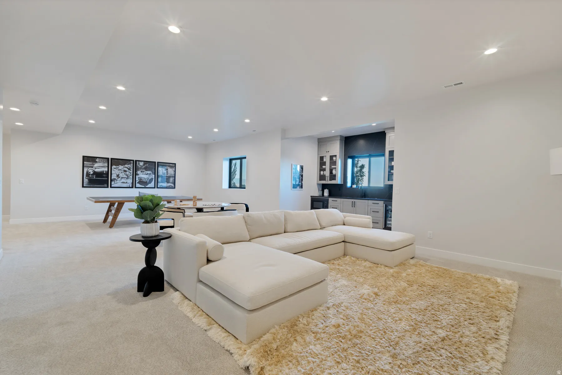 Living area featuring light colored carpet, recessed lighting, and bar with sink