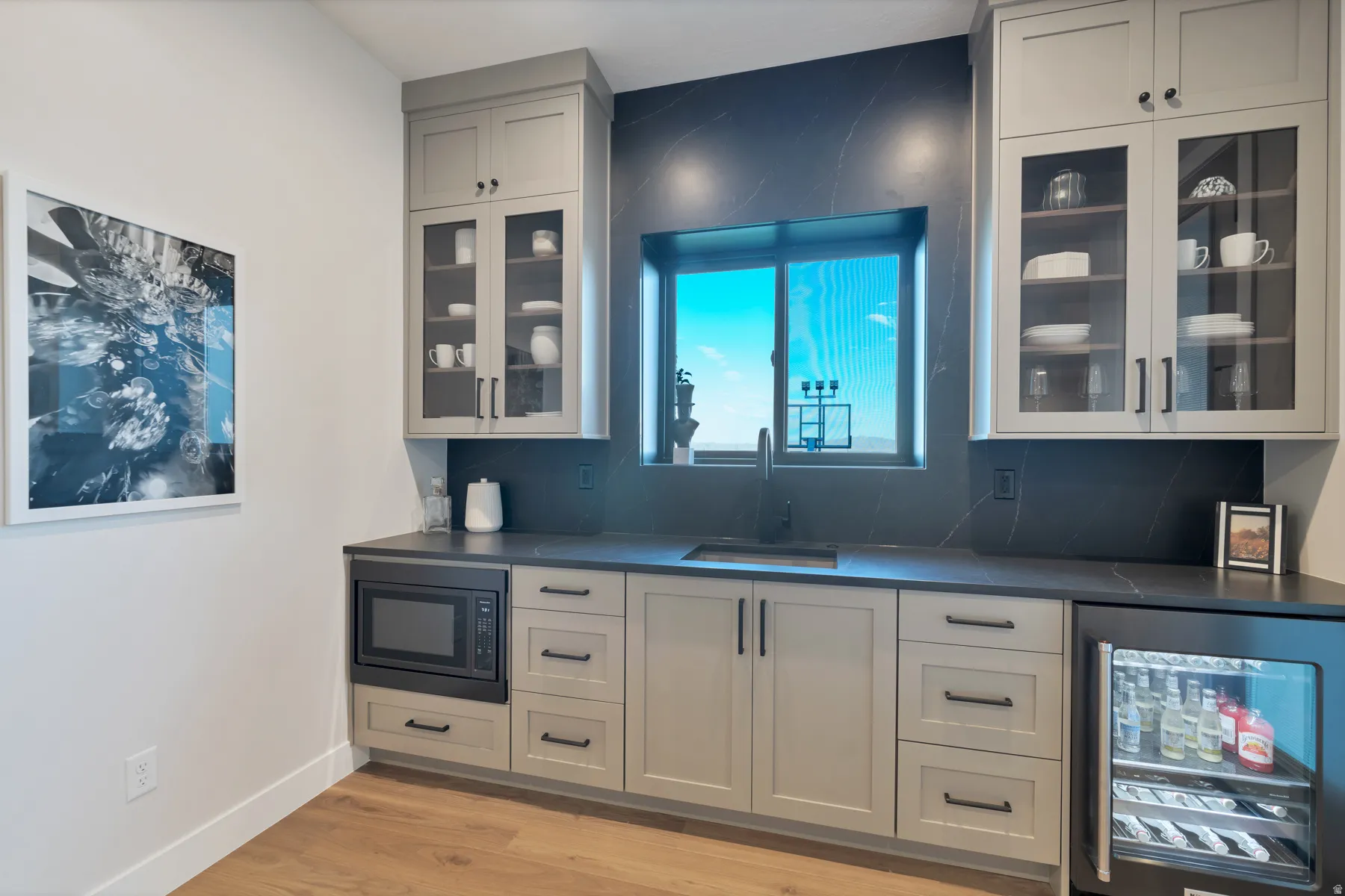 Bar area with glass fronted cabinets, beverage cooler, light wood-style floors, backsplash, and black microwave