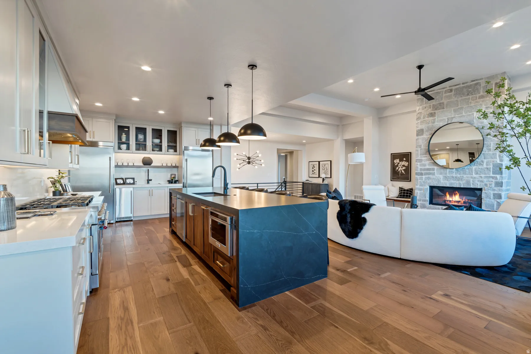 Dual tone kitchen with dark wood-type flooring, a stone fireplace, premium appliances, hanging light fixtures, and dual tone cabinets