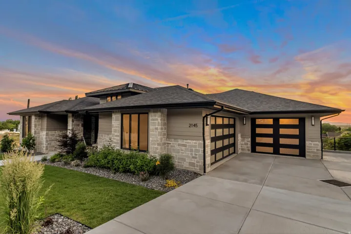 Prairie-style home with roof with shingles, an attached garage, driveway, stone siding, and a front lawn