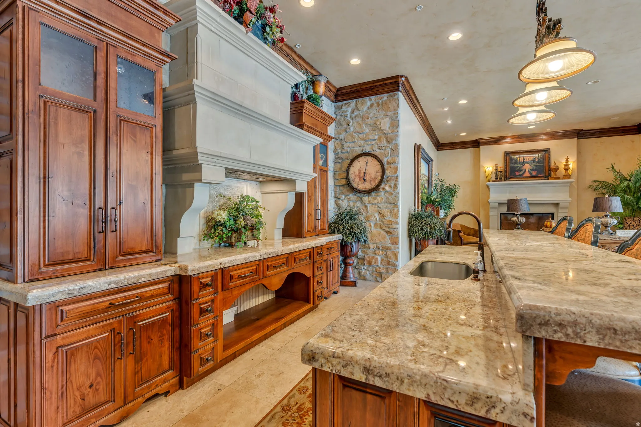 Kitchen featuring a fireplace, light stone counters, a kitchen bar, wood finish cabinets, and decorative light fixtures