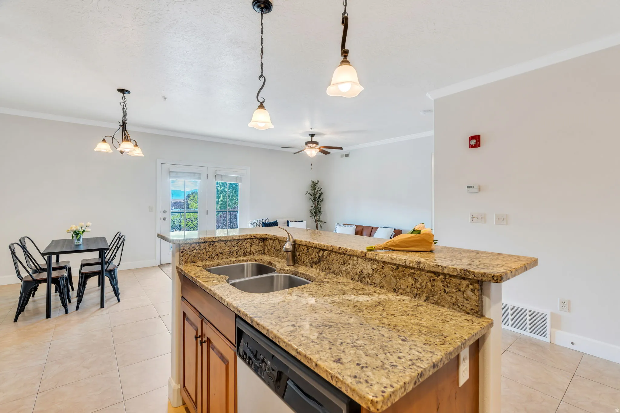 Kitchen with light stone countertops, a ceiling fan, an island with sink, wood finish cabinets, and light tile patterned floors