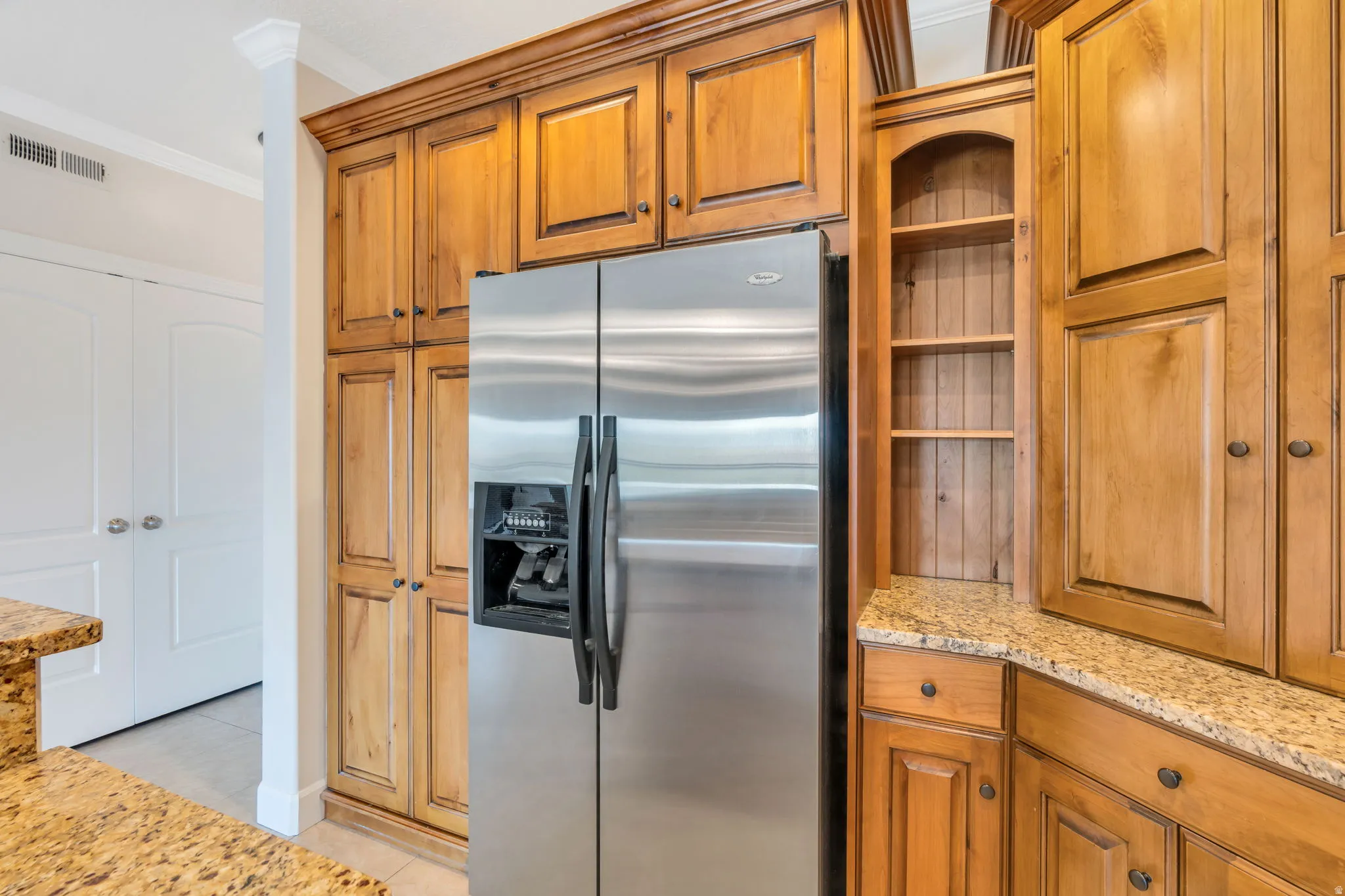 Kitchen with stainless steel fridge, wood finish cabinetry, light stone counters, and ornamental molding