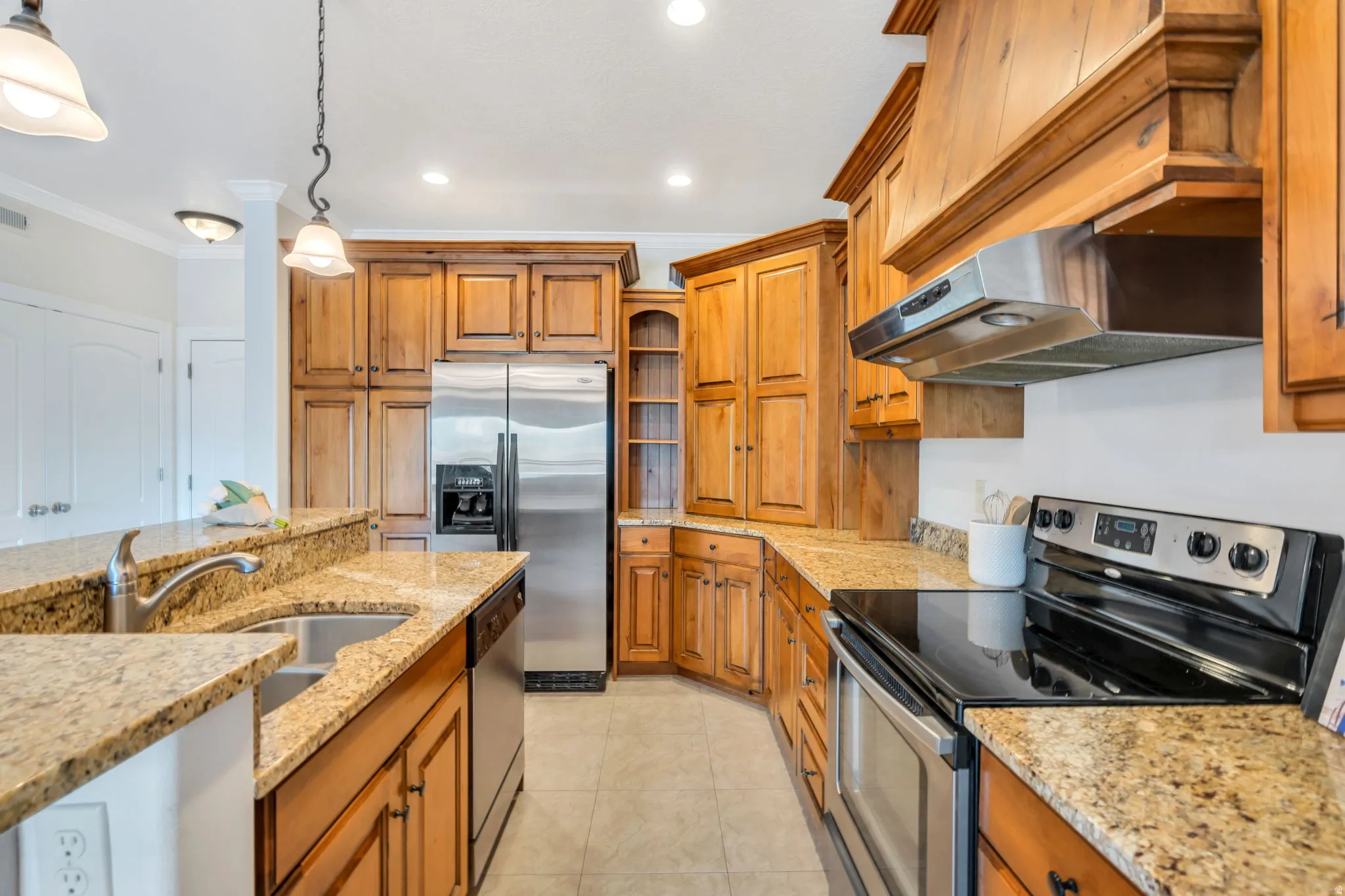 Kitchen with stainless steel appliances, light stone countertops, ornamental molding, and wood finish cabinetry
