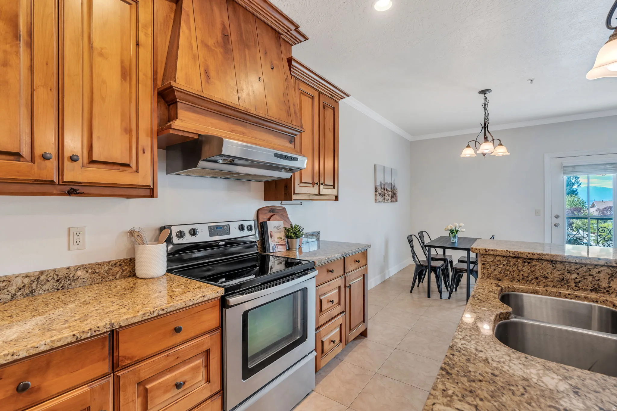 Kitchen with stainless steel range with electric stovetop, light stone counters, wood finish cabinets, crown molding, and light tile patterned floors