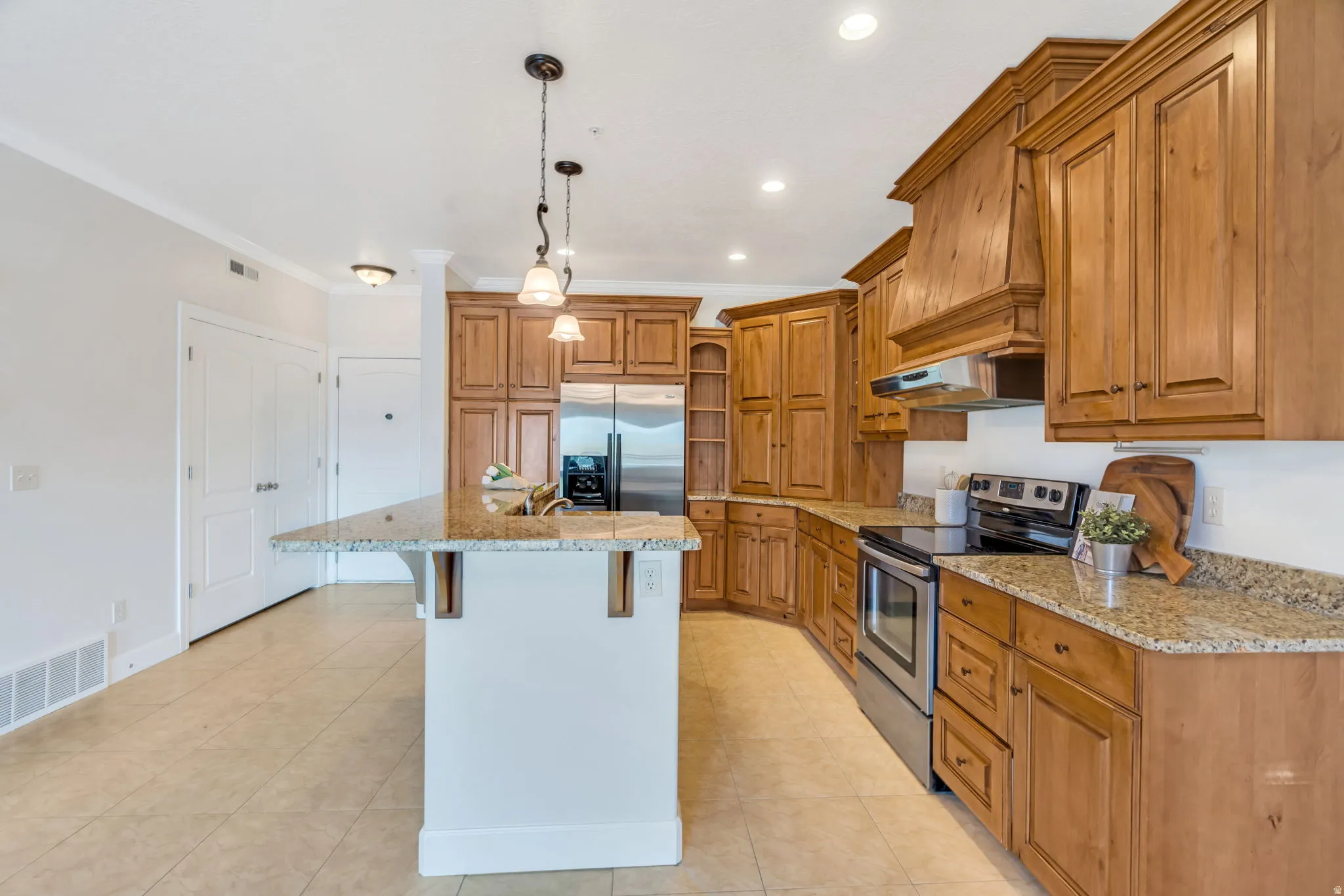 Kitchen featuring wood finish cabinetry, stainless steel appliances, a center island with sink, a breakfast bar, and light stone counters