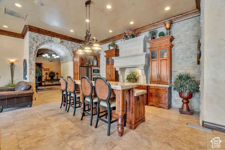 Kitchen featuring wood finish cabinets, arched walkways, a kitchen bar, ornamental molding, and glass fronted cabinets