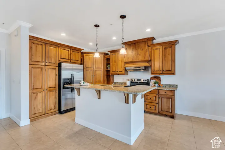 Kitchen featuring wood finish cabinets, a breakfast bar, stainless steel appliances, light stone countertops, and ornamental molding
