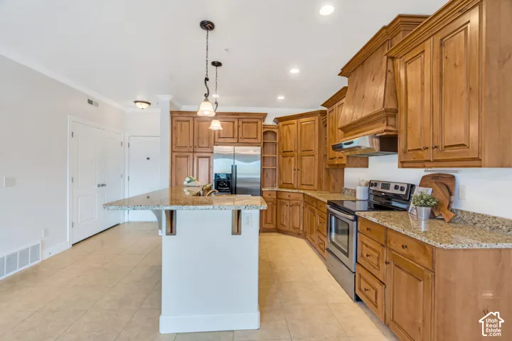 Kitchen featuring wood finish cabinetry, stainless steel appliances, a center island with sink, a breakfast bar, and light stone counters