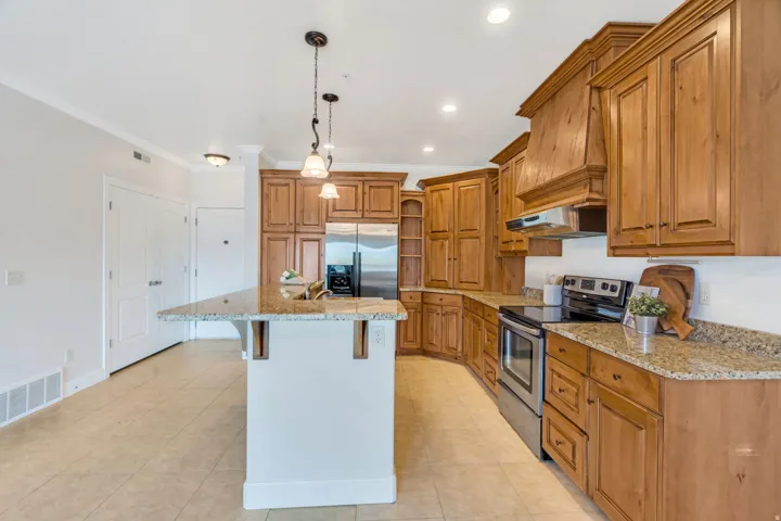 Kitchen featuring wood finish cabinetry, stainless steel appliances, a center island with sink, a breakfast bar, and light stone counters