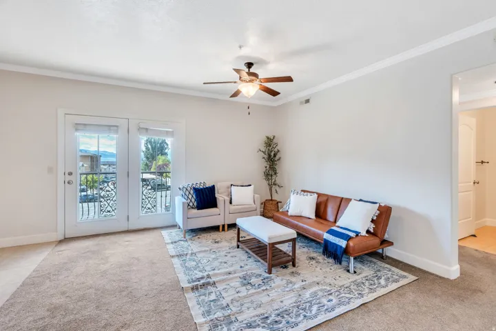 Living area featuring light carpet, ornamental molding, and a ceiling fan