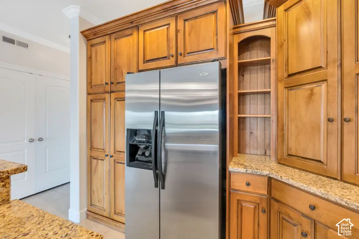 Kitchen with stainless steel fridge, wood finish cabinetry, light stone counters, and ornamental molding