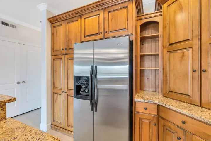 Kitchen with stainless steel fridge, wood finish cabinetry, light stone counters, and ornamental molding