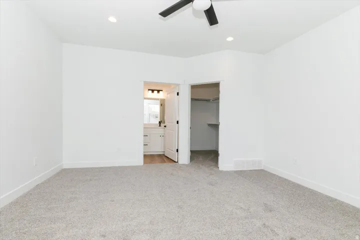 Unfurnished bedroom featuring a walk in closet, light carpet, recessed lighting, ceiling fan, and connected bathroom