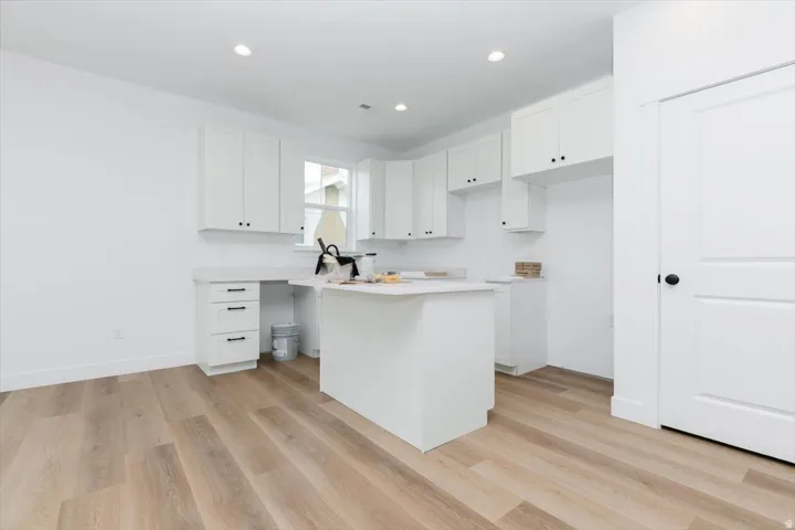 Kitchen featuring white cabinets, light wood-type flooring, light countertops, recessed lighting, and a center island