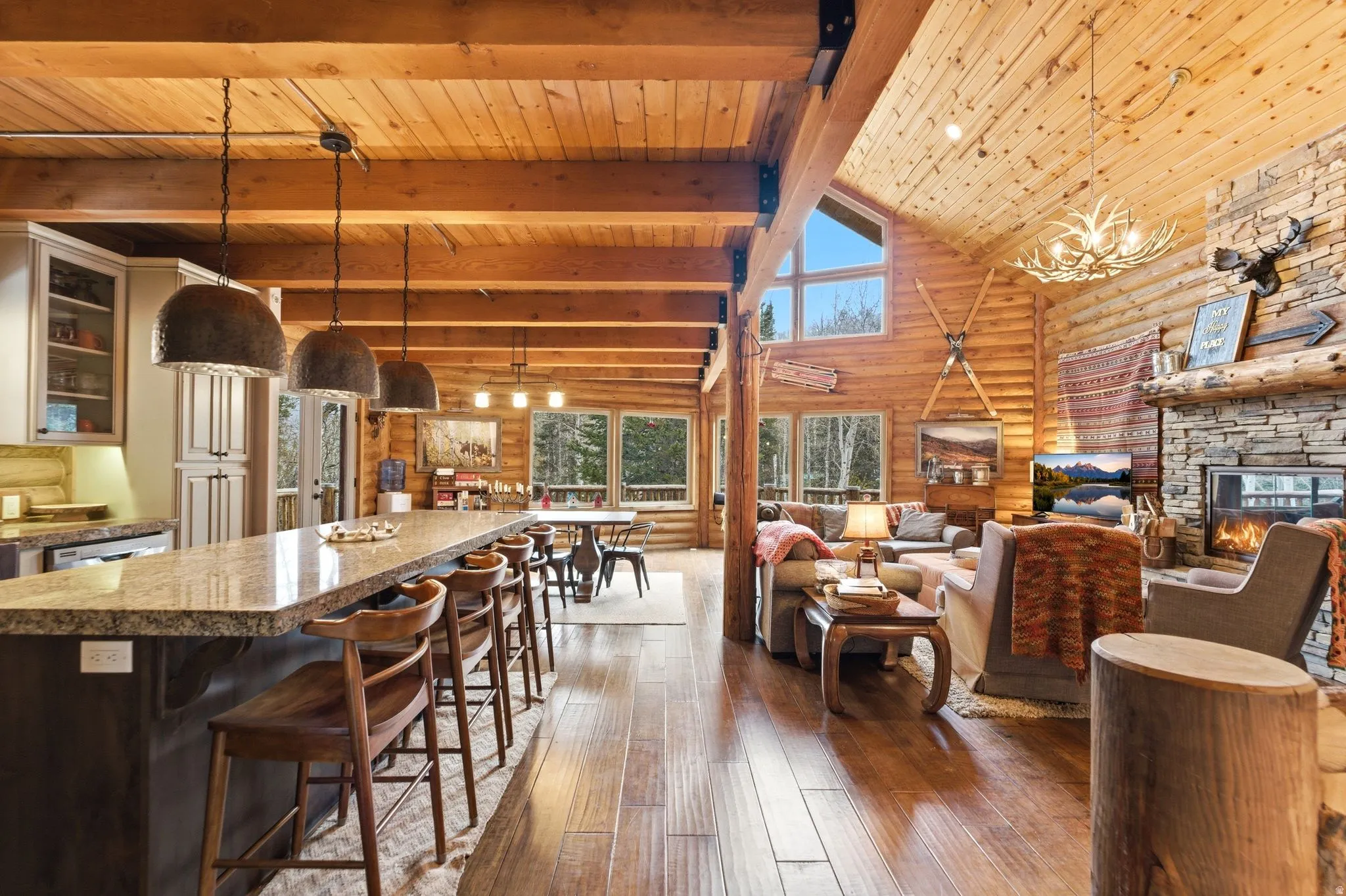 Living room with log walls, dark wood-style floors, a high wood beamed ceiling, a stone fireplace, and a chandelier