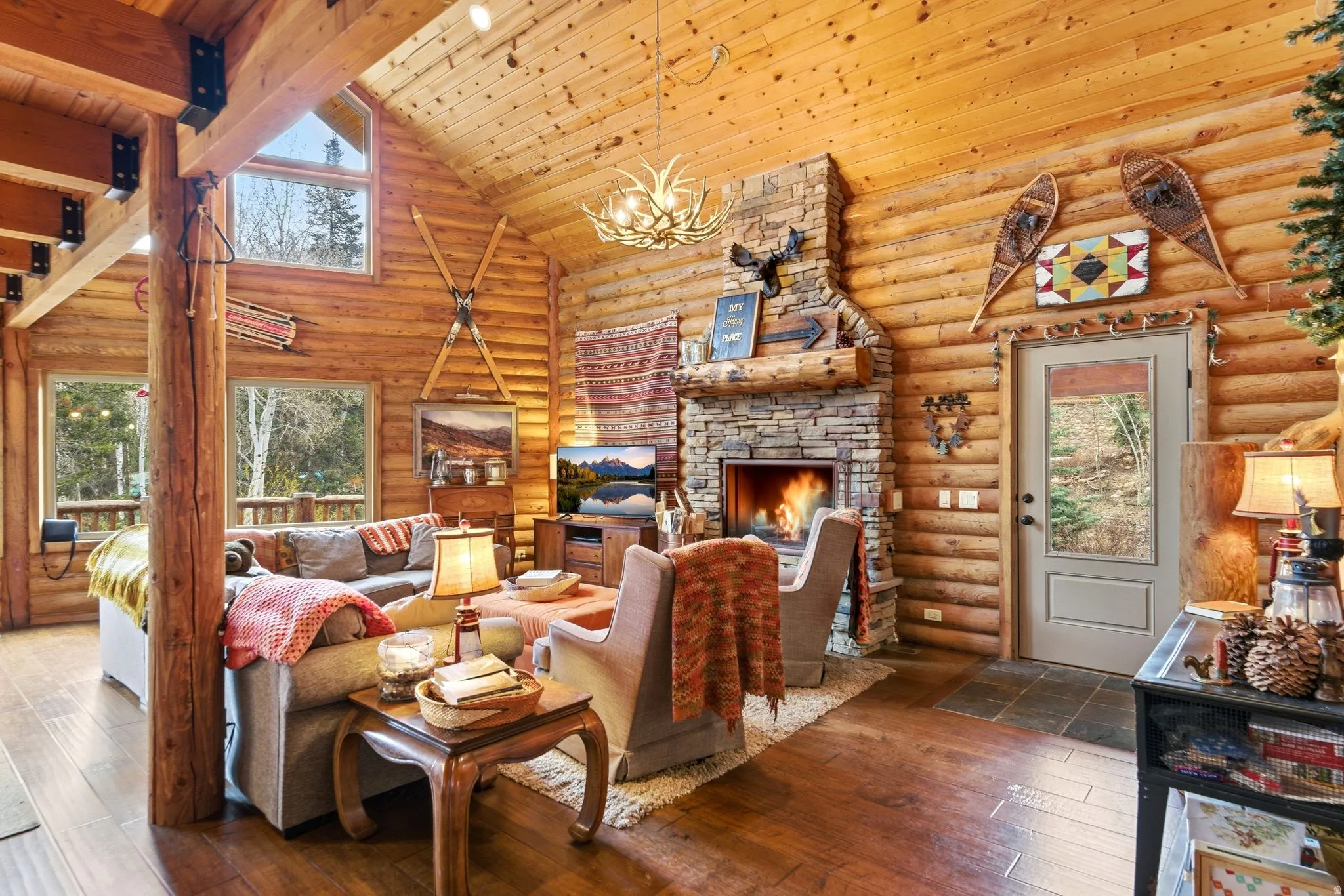 Living area featuring dark wood-type flooring, a stone fireplace, a high wooden beamed ceiling, a chandelier, and log walls