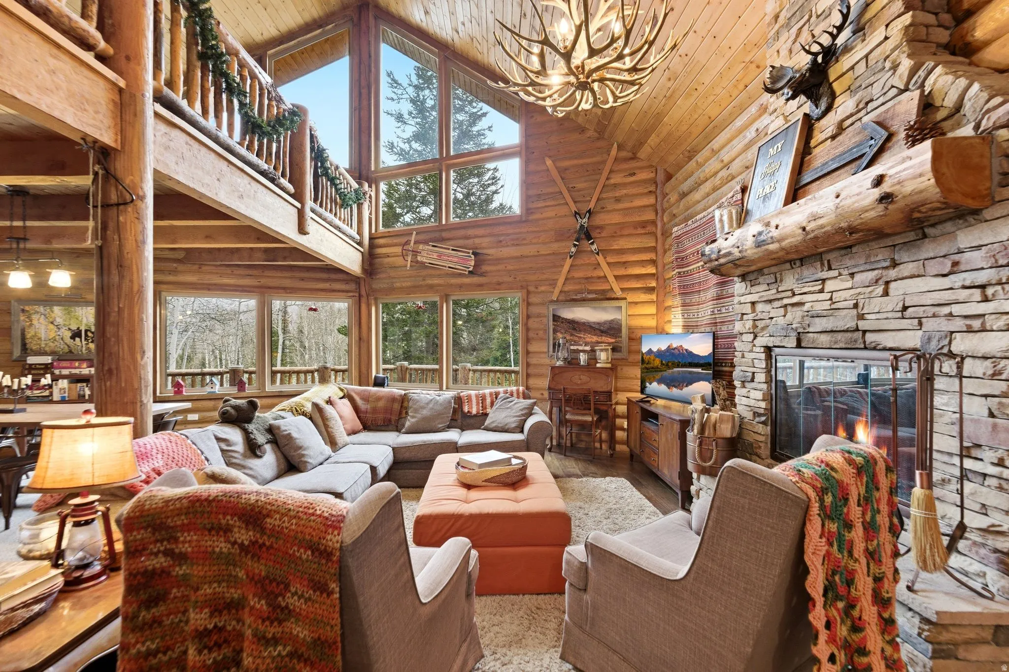 Living room featuring a vaulted wood ceiling, a fireplace, suspended lighting, rustic walls, and wood finished floors